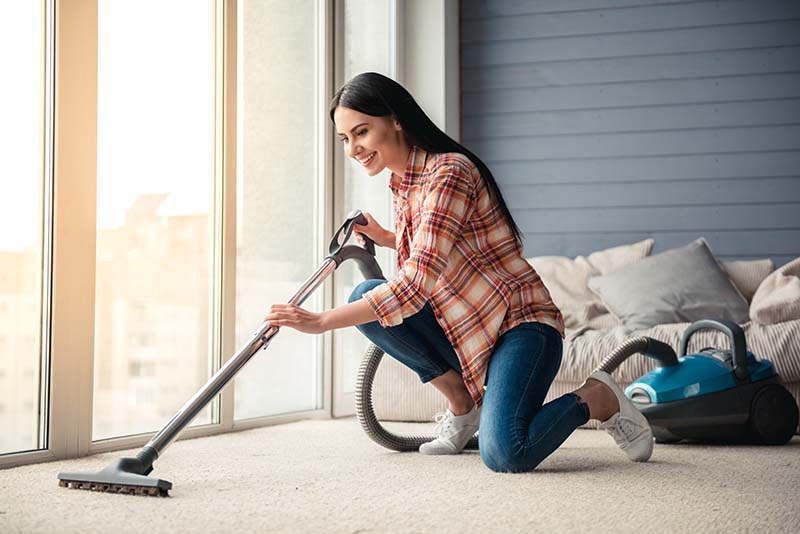 Beautiful Young Woman Vacuuming Floor at Home